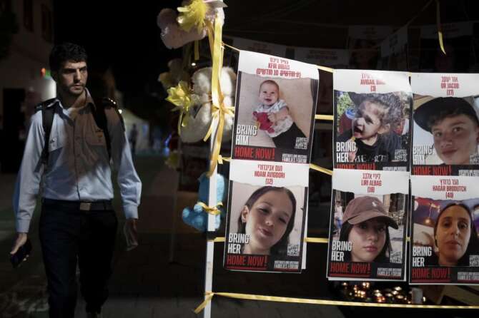 A member of Israeli security forces looks at posters of children held hostage by Hamas in the Gaza Strip, displayed ahead of an anticipated hostage release, in Tel Aviv, Israel, Thursday, Nov. 23, 2023. (AP Photo/Maya Alleruzzo)