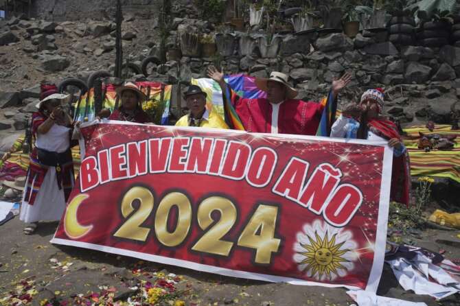 Shamans perform an annual ritual to predict political and social issues for the new year on the top of San Cristóbal hill in Lima, Peru, Wednesday, Dec. 27, 2023. The sign reads in Spanish “Welcome year 2024.” (AP Photo/Guadalupe Pardo)