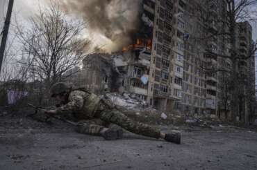 A Ukrainian police officer takes cover in front of a burning building that was hit in a Russian airstrike in Avdiivka, Ukraine, Friday, March 17, 2023. (AP Photo/Evgeniy Maloletka)