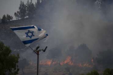 An Israeli flag flutters next to a fire burning in an area near the border with Lebanon, northern Israel in Safed, Wednesday, June 12, 2024. Scores of rockets were fired from Lebanon toward northern Israel on Wednesday morning, hours after Israeli airstrikes killed four officials from the militant Hezbollah group including a senior military commander. (AP Photo/Leo Correa)