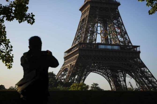 A man takes photographs of the Olympic rings mounted on the Eiffel Tower Friday, June 7, 2024 in Paris. The Paris Olympics organizers on Friday unveiled a display of the five Olympic rings mounted on the Eiffel Tower as the French capital marks 50 days until the start of the Summer Games. (AP Photo//Thomas Padilla)