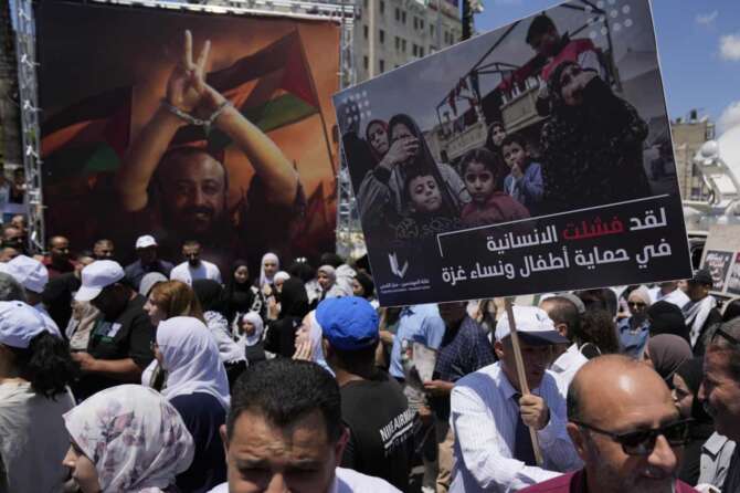 A protester carries a poster that reads “the humanity has failed in protecting the children and woman of Gaza,” in front of a big poster of Marwan Barghouti, the highest profile Palestinian prisoner held by Israel, during a rally in solidarity with Gaza and prisoners held by Israel, in the West Bank city of Ramallah, Saturday, Aug. 3, 2024. (AP Photo/Nasser Nasser)