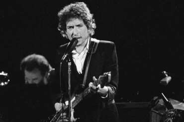 FILE – Musician Bob Dylan performs with The Band at the Forum in Los Angeles on Feb. 15, 1974. Transcripts of lost 1971 Dylan interviews with the late American blues artist Tony Glover and letters the two exchanged reveal that Dylan changed his name from Robert Zimmerman because he worried about anti-Semitism, and that he wrote “Lay Lady Lay” for actress Barbra Streisand. The items are among a trove of Dylan archives being auctioned in November 2020 by Boston-based R.R. Auction. (AP Photo/Jeff Robbins, File)