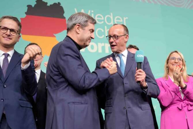 Friedrich Merz, with the microphone, the candidate of the mainstream conservative Christian Democratic Union party, shakes hands with Markus Soeder, leader of CSU and Minister-President of Bavaria, at the party headquarters in Berlin, Germany, Sunday, Feb. 23, 2025, after the German national election. (AP Photo/Markus Schreiber)