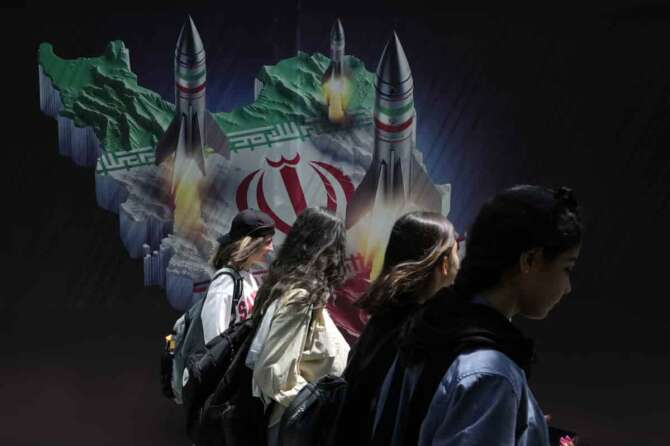 Iranian women without wearing their mandatory Islamic headscarf walk past a banner showing missiles being launched from Iranian map in northern Tehran, Iran, Friday, April 19, 2024. Iran fired air defenses at a major air base and a nuclear site near the central city of Isfahan after spotting drones early Friday morning, raising fears of a possible Israeli strike in retaliation for Tehran’s unprecedented drone-and-missile assault on the country. (AP Photo/Vahid Salemi)
