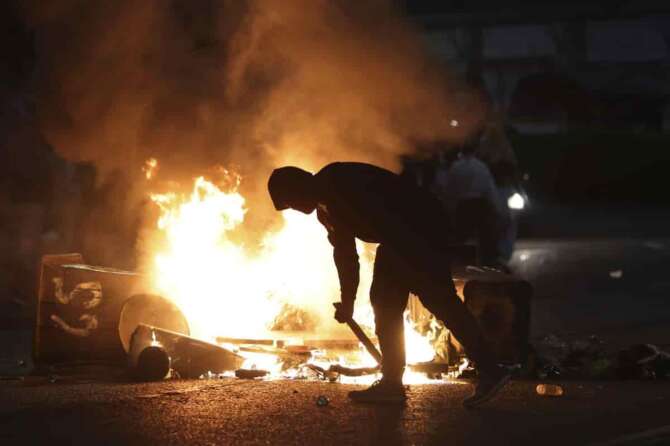 A protester stokes a barricade fire in Ballymena, Northern Ireland, as people protest over an alleged sexual assault in the Co Antrim town, Wednesday, June 11, 2025. (AP Photo/Peter Morrison)