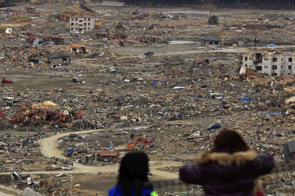 FILE – In the March 21, 2011, file photo, people look out at the tsunami damage from a hill where there is a shelter set up in a school in Minamisanriku, northern Japan. The earthquake and the tsunami it generated on March 11, 2011, killed about 18,000 people and devastated the coastline. Buildings in Minamisanriku were flattened, and more than 800 people in the city were killed or went missing. (AP Photo/Matt Dunham, File)