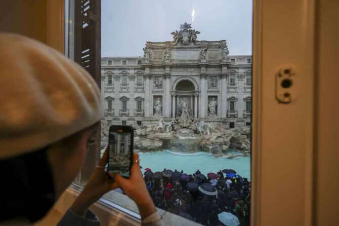 A woman takes a picture of the 18th century Trevi Fountain, one of Rome’s most iconic landmarks, as it reopens to the public after undergoing maintenance, just on time for the start of the Jubilee Year, an event expected to draw millions of visitors to the Eternal City, in Rome, Sunday, Dec. 22, 2024. (AP Photo/Andrew Medichini)