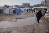 Palestinians walk through a flooded area in a temporary tent camp after heavy rainfall in Deir al-Balah, central Gaza Strip, Friday, Dec. 12, 2025. (AP Photo/Abdel Kareem Hana)