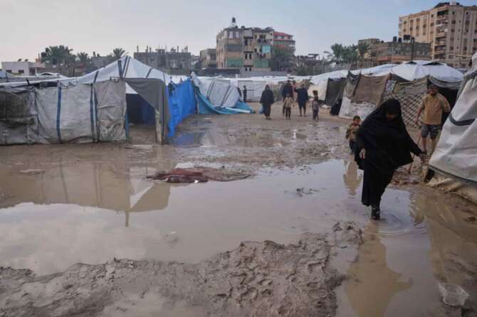 Palestinians walk through a flooded area in a temporary tent camp after heavy rainfall in Deir al-Balah, central Gaza Strip, Friday, Dec. 12, 2025. (AP Photo/Abdel Kareem Hana)
