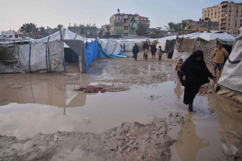 Palestinians walk through a flooded area in a temporary tent camp after heavy rainfall in Deir al-Balah, central Gaza Strip, Friday, Dec. 12, 2025. (AP Photo/Abdel Kareem Hana)
