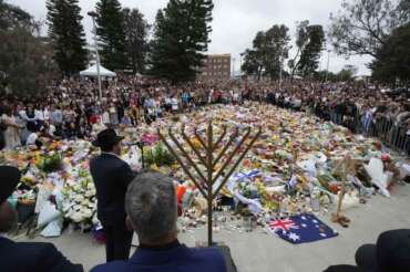 Rabbi Motti Feldman, lower left, speaks at a menorah lighting ceremony at a floral memorial for victims of Sunday’s shooting, at the Bondi Pavilion at Bondi Beach on Tuesday, Dec. 16, 2025, in Sydney, Australia. (AP Photo/Mark Baker)