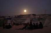 The moon rises behind a tent camp for displaced Palestinians along the Muwasi, an area that Israel has designated as a safe zone, in Khan Younis southern Gaza Strip Tuesday, Oct. 7, 2025. (AP Photo/Jehad Alshrafi)