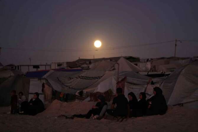 The moon rises behind a tent camp for displaced Palestinians along the Muwasi, an area that Israel has designated as a safe zone, in Khan Younis southern Gaza Strip Tuesday, Oct. 7, 2025. (AP Photo/Jehad Alshrafi)