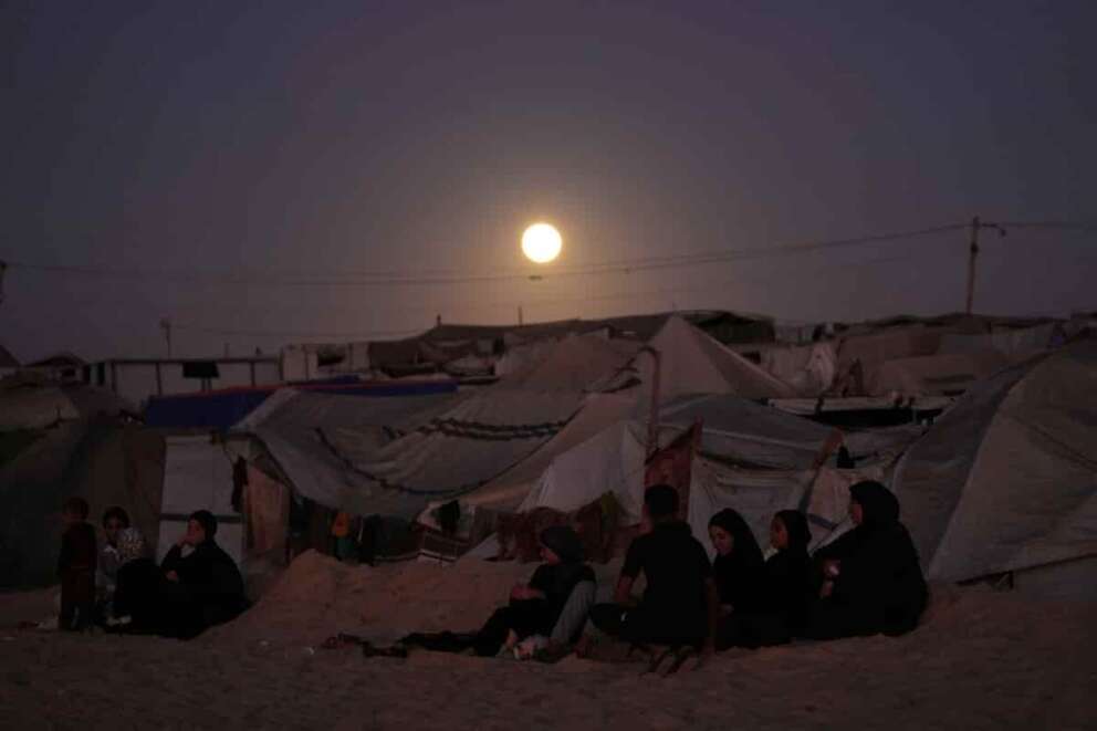 The moon rises behind a tent camp for displaced Palestinians along the Muwasi, an area that Israel has designated as a safe zone, in Khan Younis southern Gaza Strip Tuesday, Oct. 7, 2025. (AP Photo/Jehad Alshrafi)