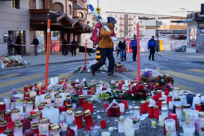 A skier passes candles near the sealed off Le Constellation bar in Crans-Montana, Swiss Alps, Switzerland, Saturday, Jan. 3, 2026, where a devastating fire left dead and injured during the New Year’s celebrations. (AP Photo/Baz Ratner)
