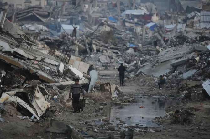 Palestinians walk amid buildings destroyed by Israeli air and ground operations in Gaza City, Tuesday, Jan. 6, 2026. (AP Photo/Jehad Alshrafi)