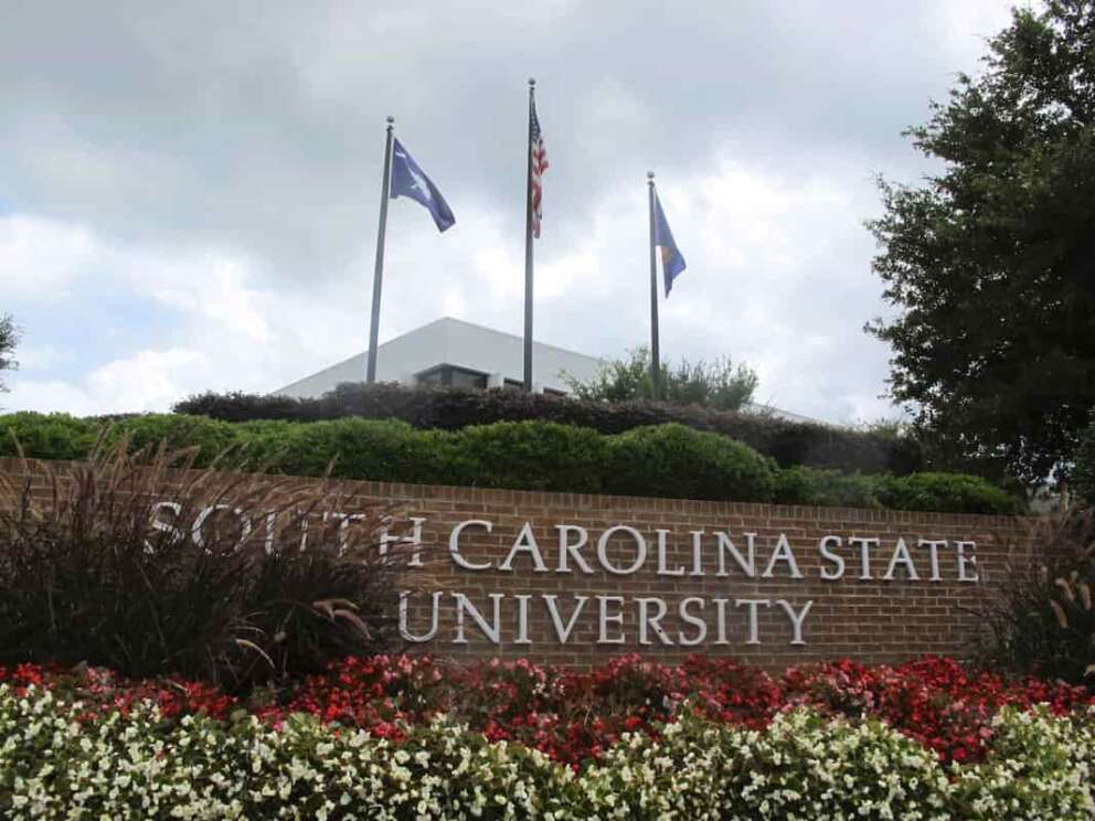 FILE – In this July 22, 2014, file photo, flags fly at the entrance to South Carolina State University in Orangeburg, S.C. A student faces charges after a shooting at South Carolina State University on Tuesday, Feb. 6, 2024 that sent the campus into lockdown for nearly one hour but did not leave any reported injuries. (AP Photo/Bruce Smith, File)