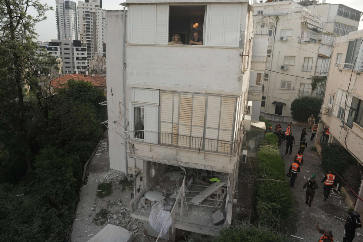 Residents watch Israeli security forces inspect the site of an Iranian missile strike in Ramat Gan, Israel, Wednesday, March 18, 2026. (AP Photo/Oded Balilty)
