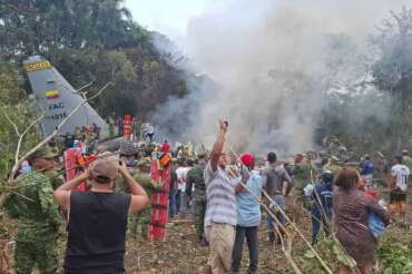 People stand around a military cargo plane that crashed after taking off from Puerto Leguizamo, Colombia, a remote municipality in the Amazonian province of Putumayo, Monday, March 23, 2026. (MiPutumayo via AP)