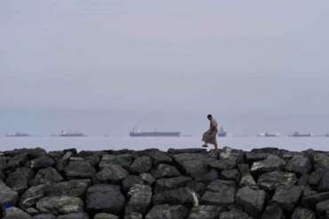 A man walks on rocks along the shore as oil tankers and cargo ships line up in the Strait of Hormuz, as seen from Khor Fakkan, United Arab Emirates, Wednesday, March 11, 2026. (AP Photo/Altaf Qadri) Associated Press / LaPresse Only italy and spain