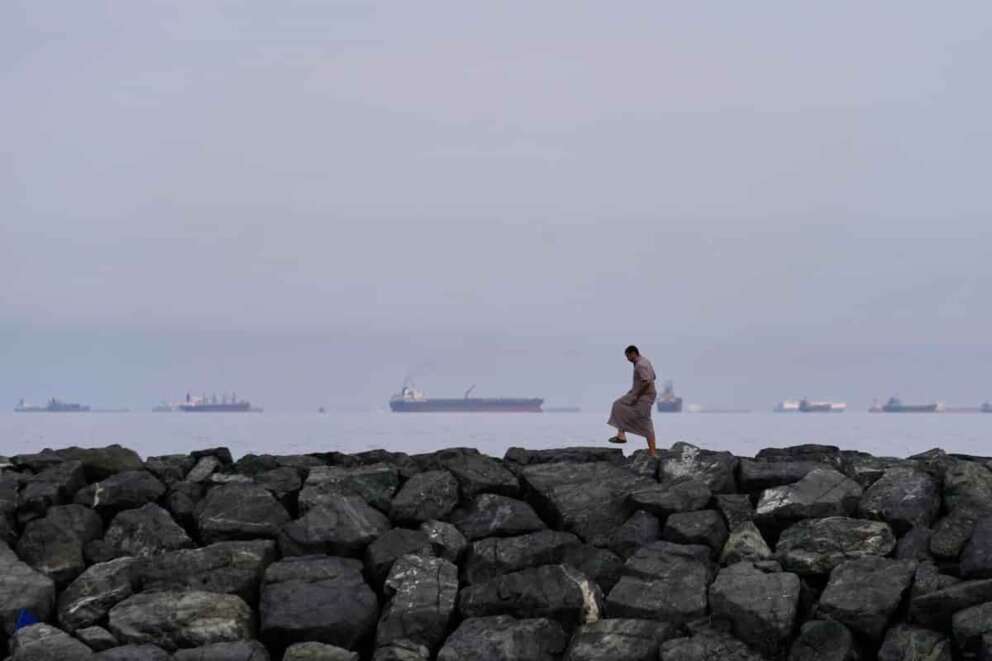 A man walks on rocks along the shore as oil tankers and cargo ships line up in the Strait of Hormuz, as seen from Khor Fakkan, United Arab Emirates, Wednesday, March 11, 2026. (AP Photo/Altaf Qadri) Associated Press / LaPresse Only italy and spain