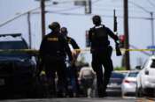 People carry weapons at the scene of a shooting outside the Islamic Center of San Diego Monday, May 18, 2026, in San Diego. (AP Photo/Gregory Bull)